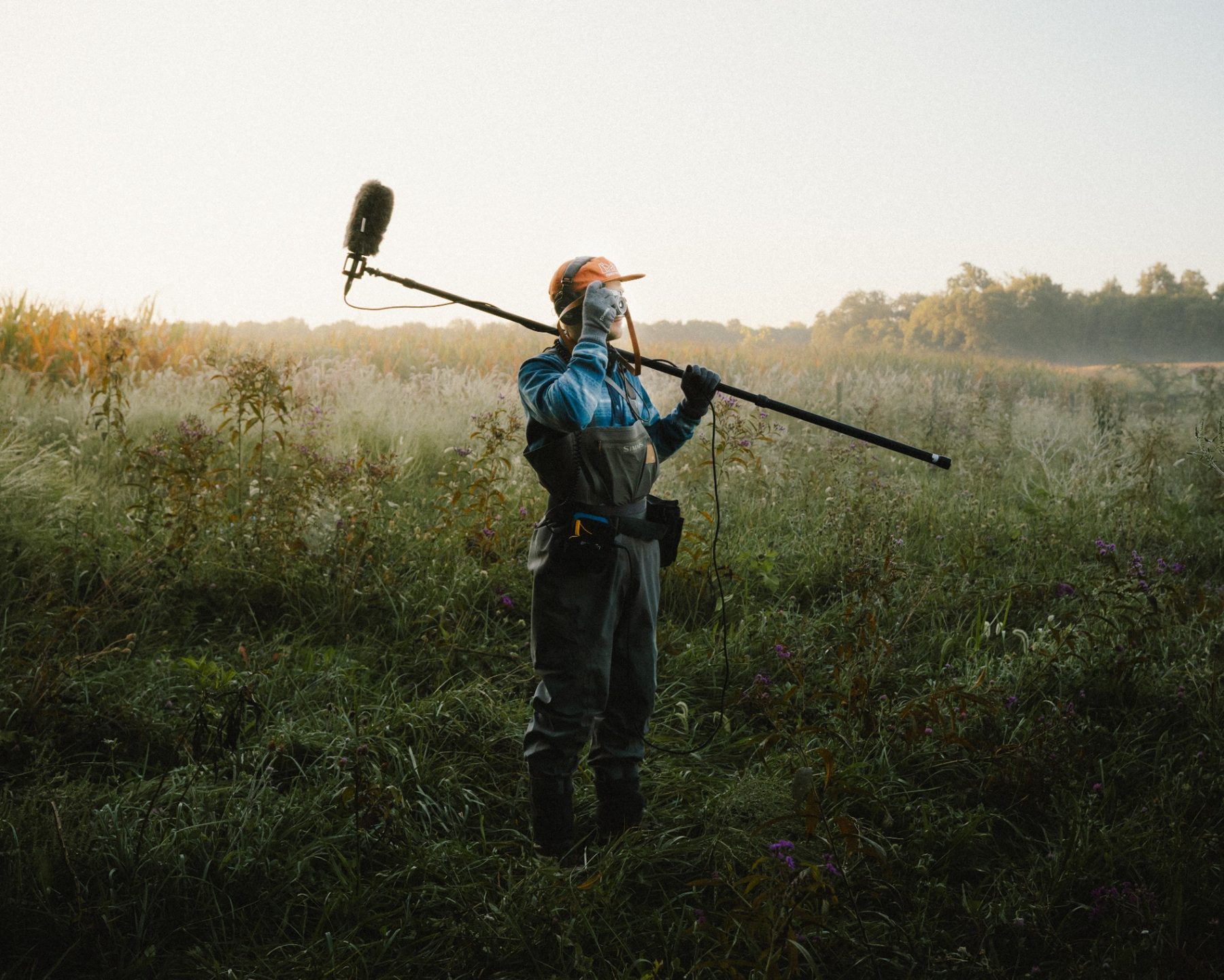 Sound recordist with boom microphone in a misty meadow at dawn